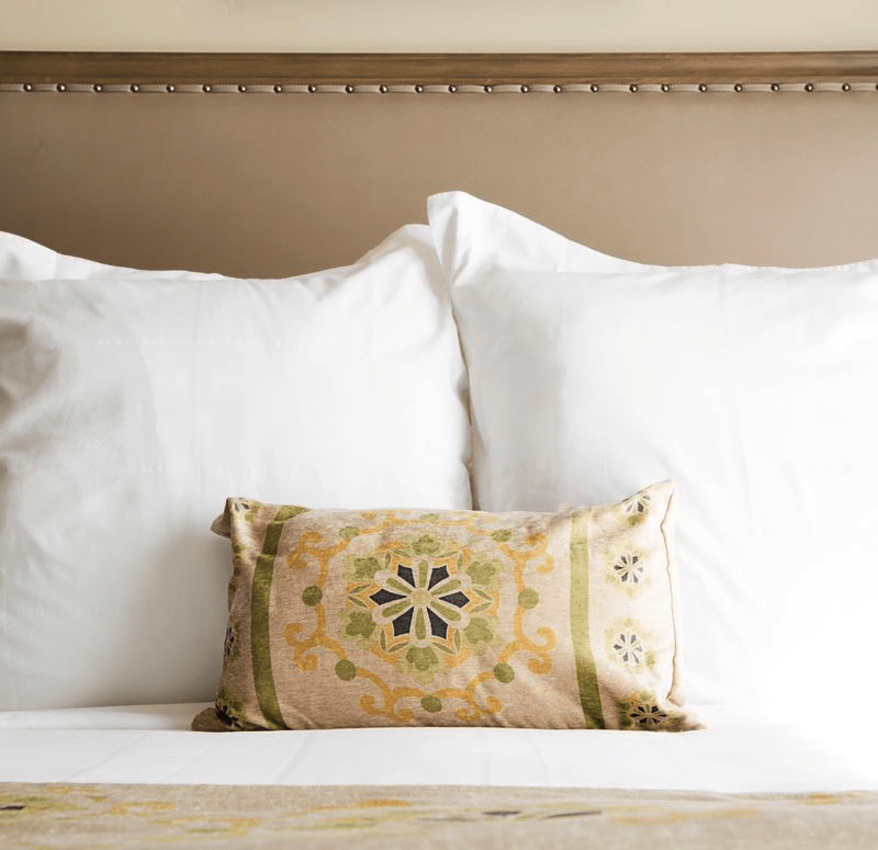 Elegant boutique hotel bed with crisp white linens and a decorative accent pillow at Ponte Vineyard Inn in Temecula Wine Country.
