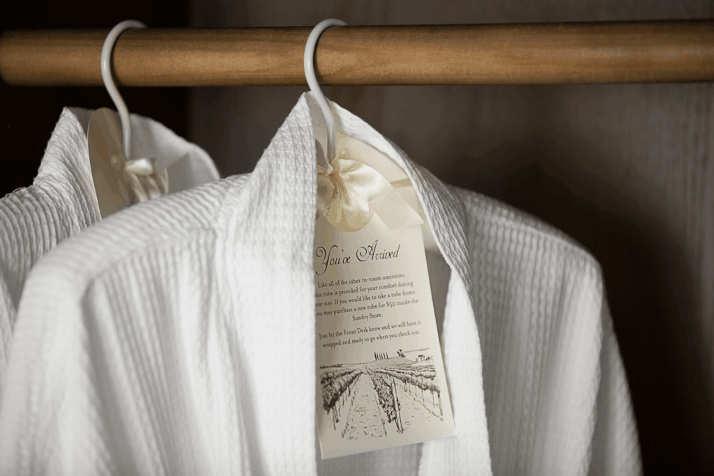 White plush robe hanging in a guest room closet at Ponte Vineyard Inn, featuring a welcome tag and vineyard illustration.